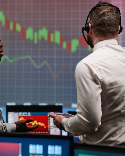 Caucasian man and his African American colleague working in stock trading company discussing currency fall